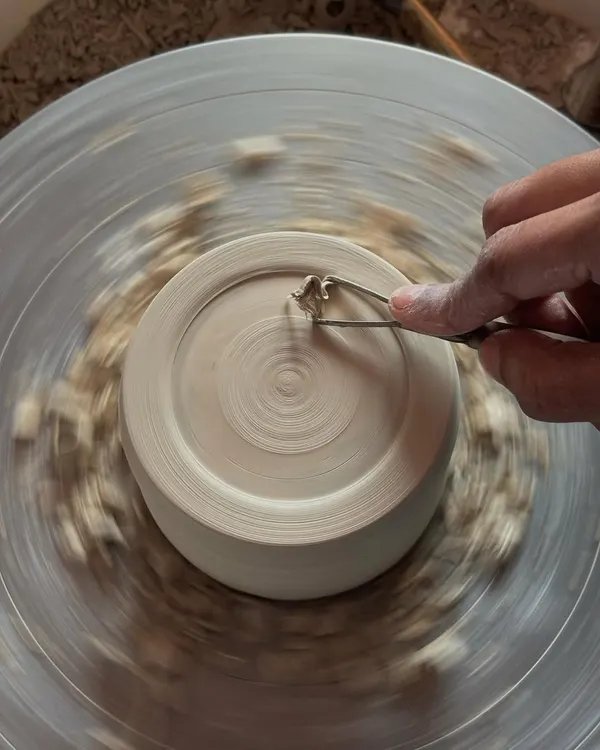 Trimming a piece on the wheel. This is a crucial step to refine the base and shape of a pot after it has hardened slightly.
