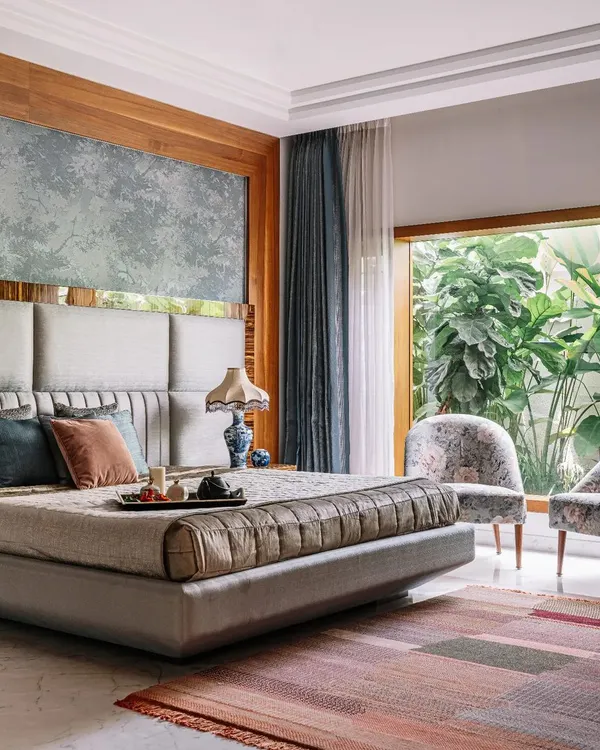 This master bedroom is a perfect example of serene luxury. The large window offers an uninterrupted view of the private garden, making you feel connected to nature. The upholstered headboard and soft, layered textiles create an inviting and restful environment.