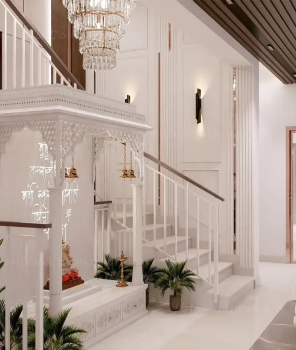 A magnificent white mandir beautifully integrated under a staircase. The intricate jali work, traditional temple design, and elegant chandelier create a divine and serene atmosphere.