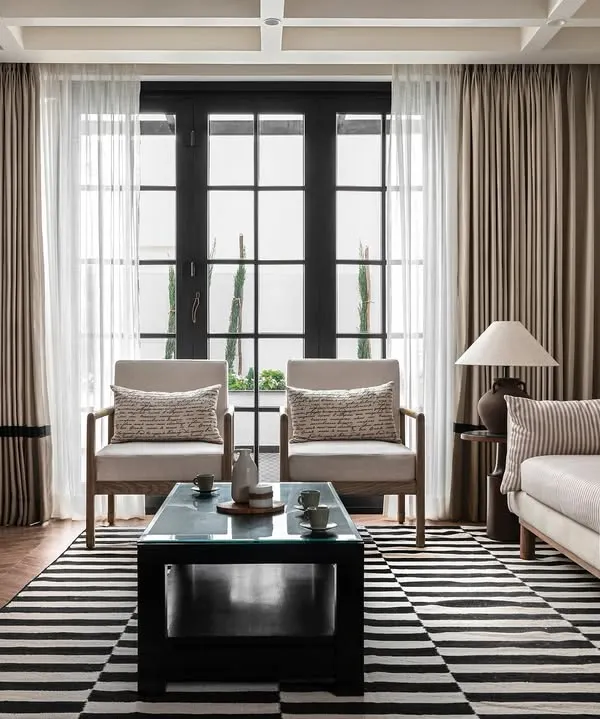 The living room of our 'Riviera Maison' project, inspired by the French Riviera. The design uses a calm, neutral palette, classic furniture silhouettes, and a bold striped rug to create a space that is both sophisticated and relaxed.