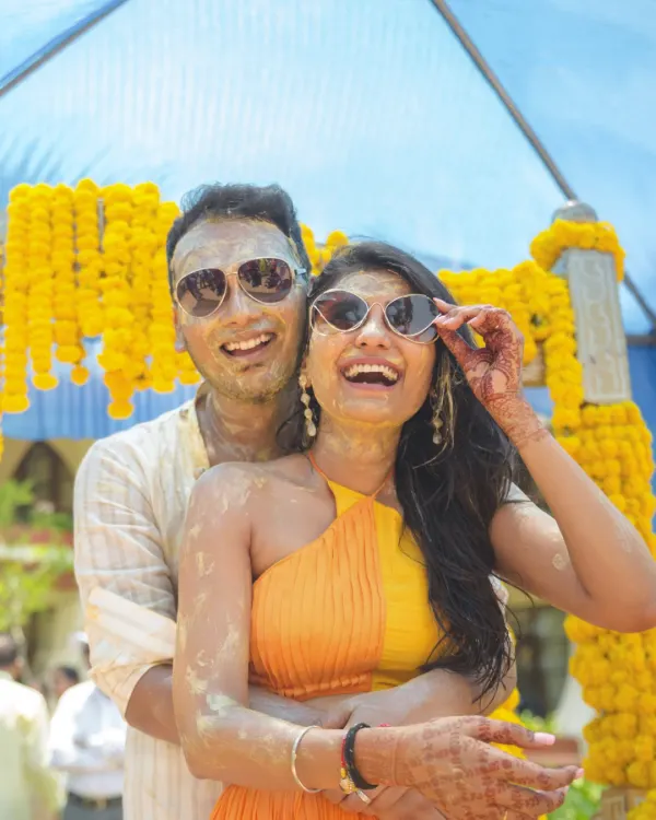 Pure fun and laughter captured during a Haldi ceremony, as the couple, covered in turmeric paste, poses with sunglasses.