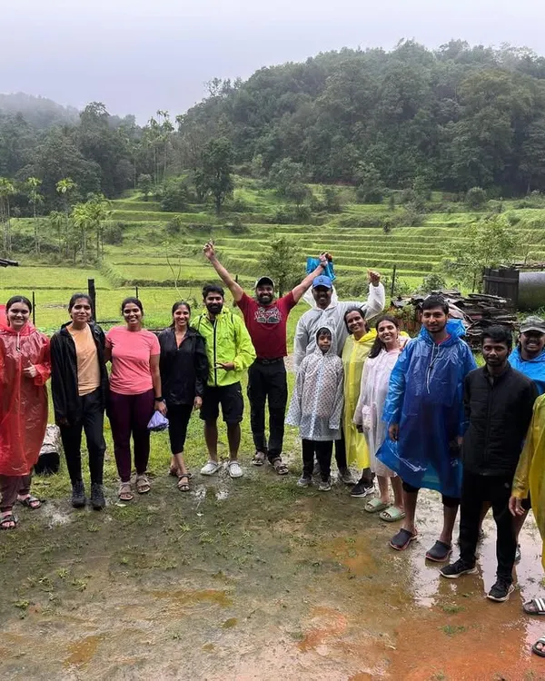 A happy group photo in the rain, standing in front of lush green paddy fields. The monsoon brings out the best smiles.