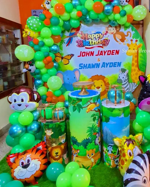 A vibrant jungle-themed birthday party setup. This decoration includes a large circular backdrop with jungle animals, themed pedestals for the cake, animal-shaped foil balloons, and a lush green balloon arch.