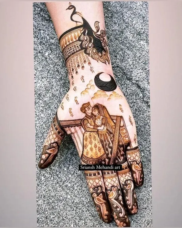 A modern and romantic Karwachauth design. It features a couple embracing under the moon, with a graceful peacock on the wrist. This is a perfect example of telling a story in a smaller space.