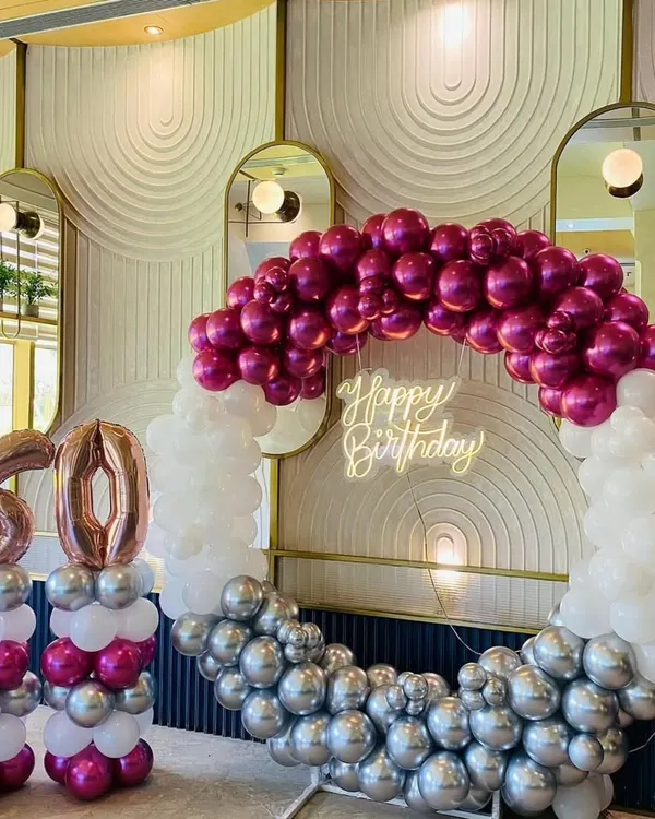 A stunning 60th birthday celebration. We used a half-and-half balloon ring with chrome magenta, white, and silver balloons, a neon sign, and large foil number balloons to create an elegant and modern photo-op area.