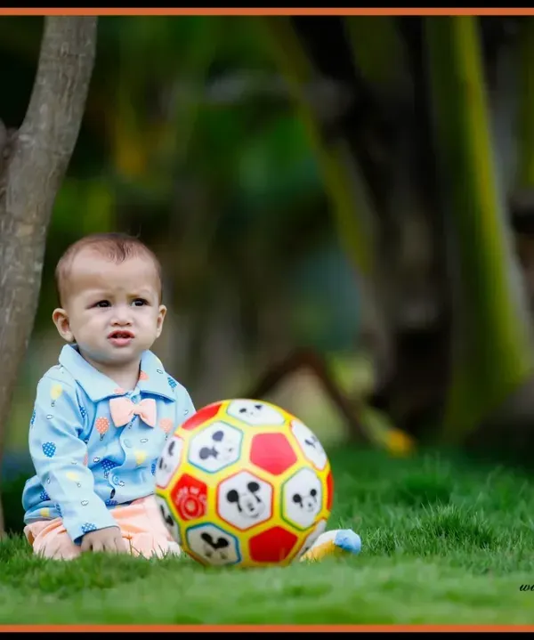 An outdoor setting is a perfect playground for a kid's photoshoot. This image captures a quiet, candid moment of a young boy with his ball in a park.