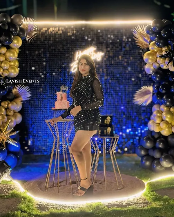 A perfect example of a modern glam setup. A sparkling shimmer wall, black and gold balloon arrangements, and a custom neon sign create a high-impact photo corner.