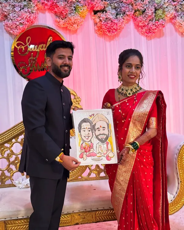 A happy couple at their wedding reception, holding a custom watercolor caricature I drew for them, capturing their traditional attire and the joy of their special day.