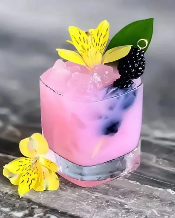 A beautifully crafted pink mocktail. This drink is garnished with an edible flower and fresh blackberries, showcasing our flair for creating visually appealing non-alcoholic beverages.