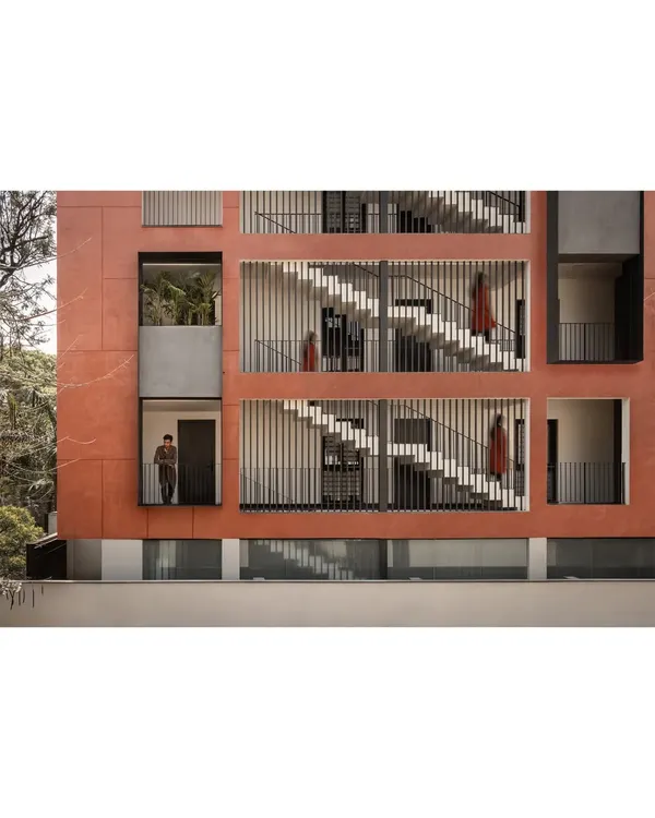 This is the facade of our "Under the Silver Oak" project. We designed the building as a monolithic deep red volume, a nod to vernacular terracotta tones, creating a bold architectural statement that interacts dynamically with the shifting shadows of the central tree.