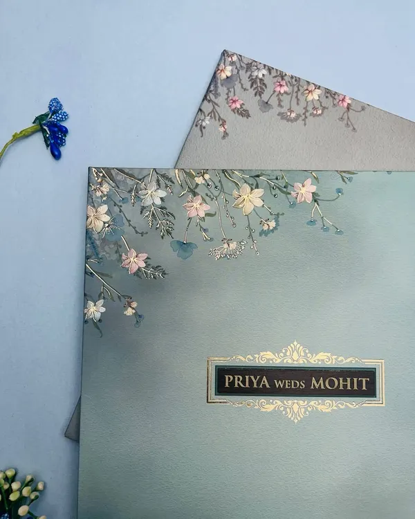 A closer look at this serene, pastel blue invitation. The delicate floral sketches and gold foil nameplate create a look of understated luxury, perfect for a modern romance.