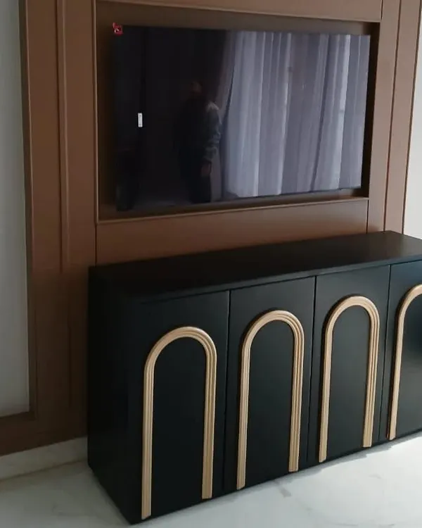 A striking black media cabinet with applied arch details in a gold finish. This piece was designed as part of a larger TV unit, providing stylishly concealed storage that complements the room's modern aesthetic.