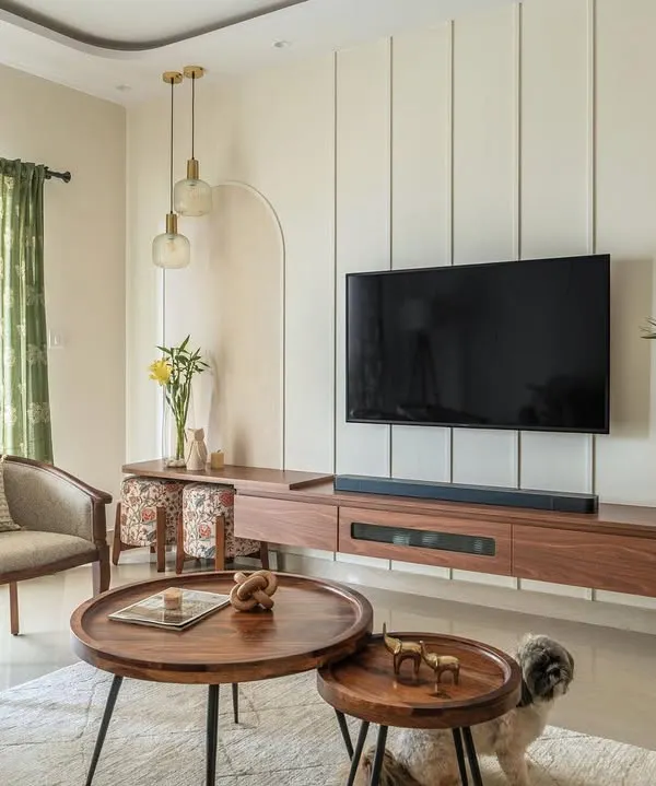 This living room from my Sobha Daffodil project balances classic and contemporary elements. A floating wooden TV unit is set against a wall with modern vertical paneling and a soft arch, creating a serene and elegant focal point.