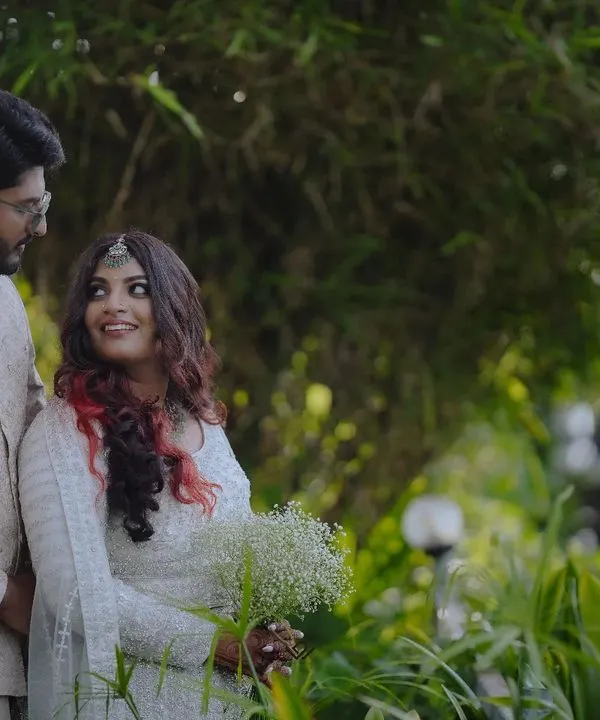 A stylish couple posing in a lush, green outdoor setting, showcasing a modern yet romantic look.