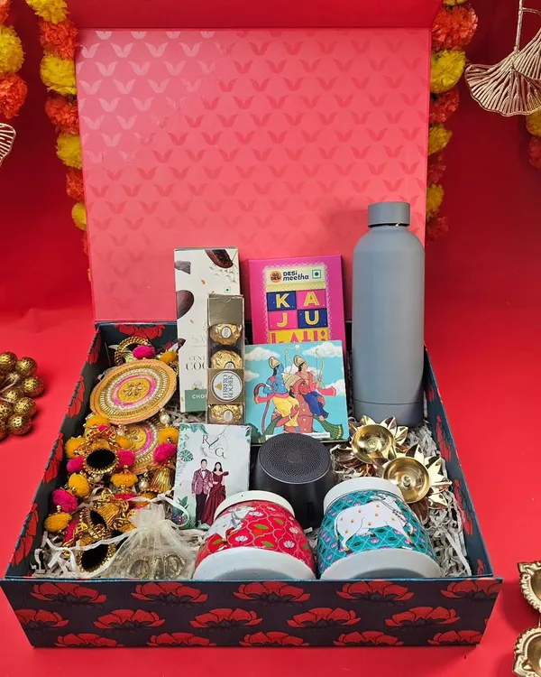 Our Diwali hampers are designed to impress. This large, patterned box is filled with a variety of goodies, including unique mugs, a water bottle, traditional torans, diyas, and sweet treats.