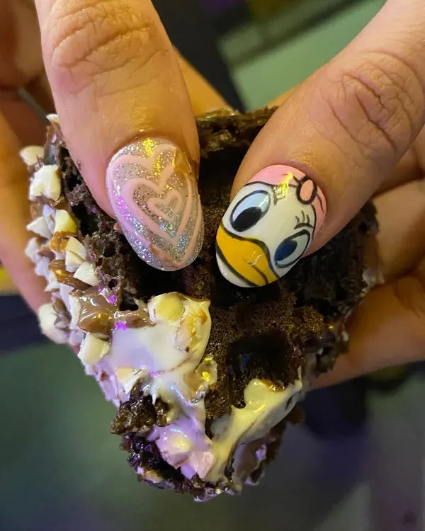 Chocolate waffle or nails? This fun design features a hand-painted Daisy Duck on one nail and a sparkling glitter heart on the other. A perfect treat for your fingertips.
