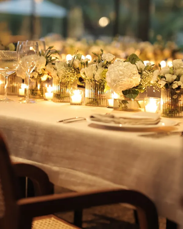 A long table dressed in white linen and bathed in candlelight creates a truly magical setting for a sit-down dinner. The rows of candles and white flowers reflect our philosophy of simple, timeless elegance.