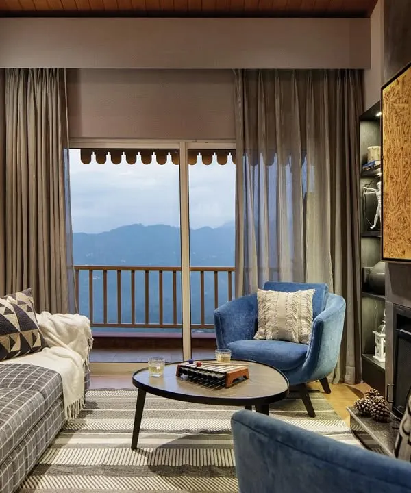 The living room is the soul of this mountain home, anchored by a hand-built fireplace and wrapped in the warmth of natural wood. We designed this space for pause and presence, with our signature Ava chairs inviting you to linger by the fire and soak in the snow-capped views.