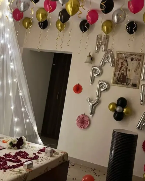 A complete romantic birthday surprise. This room decoration includes a bed canopy with fairy lights, rose petals on the bed, 'Happy Birthday' foil balloons on the wall, and balloons on the ceiling.