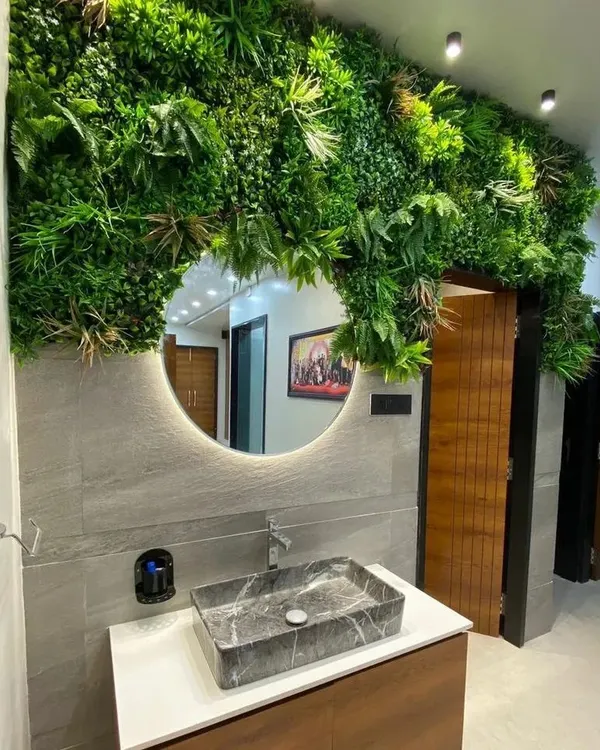 A unique bathroom vanity design featuring a vertical garden around a backlit circular mirror and a striking marble vessel sink.