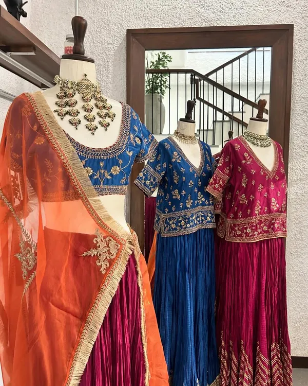 A stunning display of lehengas in jewel tones. The foreground features a blue embroidered blouse with a contrasting orange and pink skirt, perfect for a wedding guest.