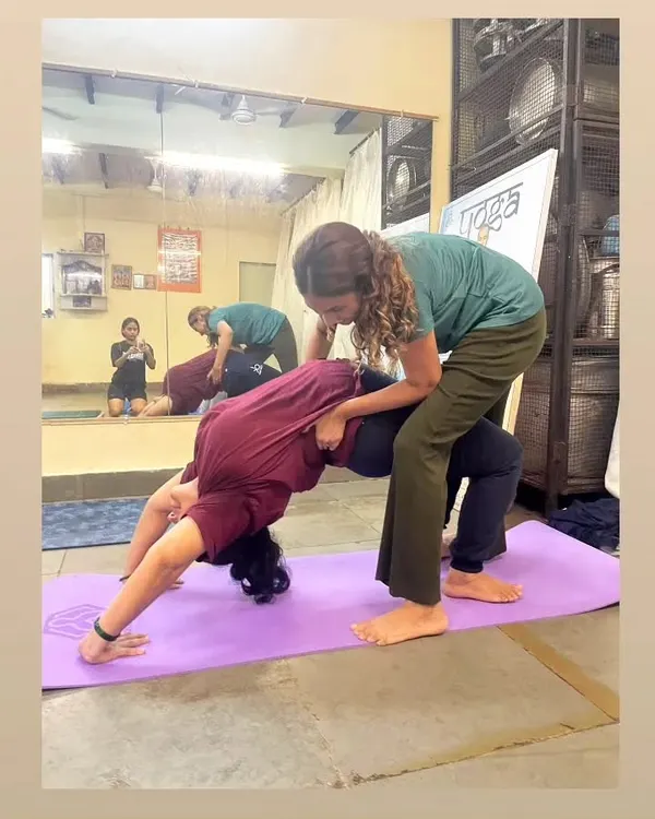 Providing hands-on assistance is key to safe practice. Here, I'm supporting a student in Wheel Pose to ensure her alignment is correct, preventing injury and helping her experience the full benefits of the asana.
