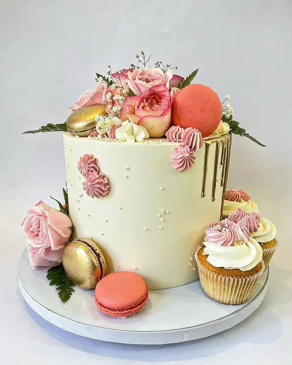 This is one of my favorite styles: simple, elegant, and unique. The tall buttercream cake is decorated with fresh pink roses, gold and pink macarons, a subtle gold drip, and coordinating cupcakes on the side.