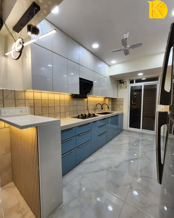 A stunning parallel kitchen from a completed project, featuring powder blue and white high-gloss acrylic cabinets, a breakfast counter with fluted paneling, and modern pendant lights. This is a perfect example of our turnkey kitchen solutions.