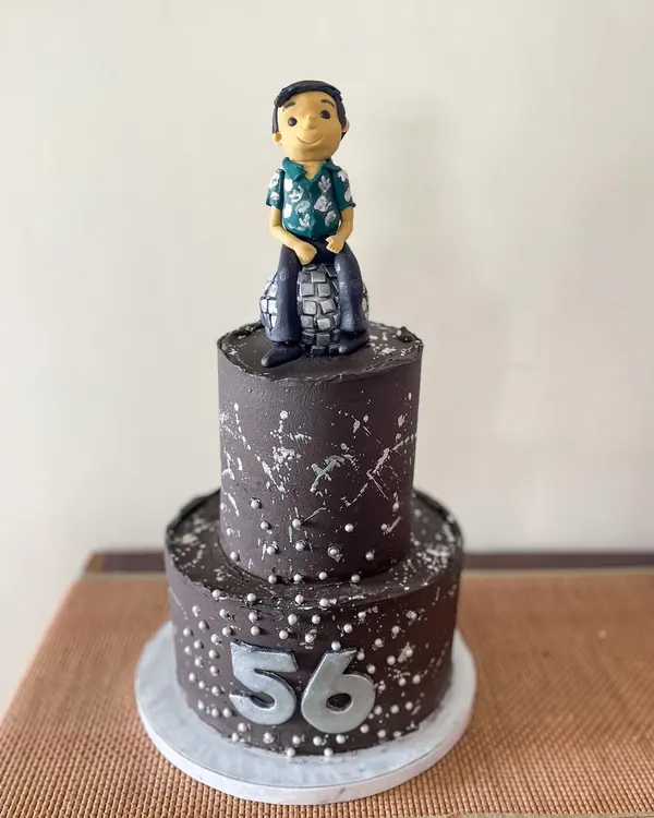 Time to boogie! This two-tiered disco-themed cake was for a 56th birthday party. It's covered in dark chocolate ganache with silver splatter and features a custom fondant figurine of the birthday guy on a disco ball.