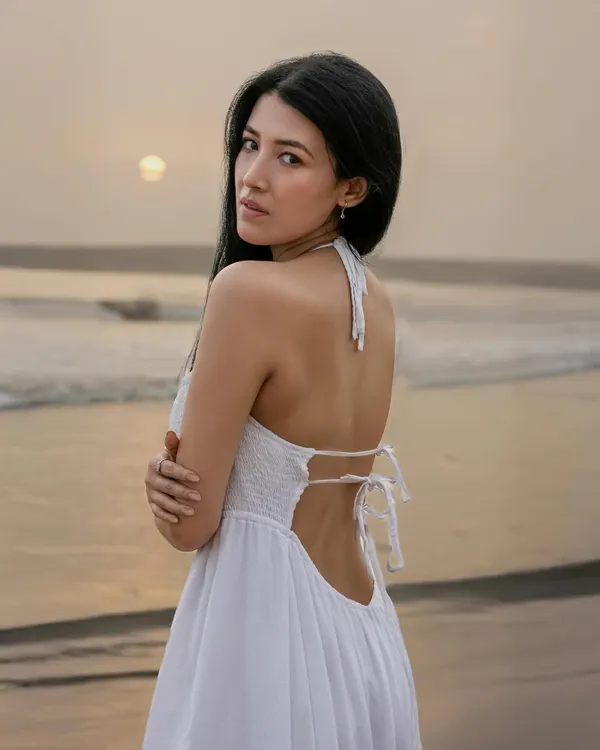 A beautiful back-shot of a model in a white dress against the setting sun. This image captures the serene and peaceful atmosphere of the beach at dusk.
