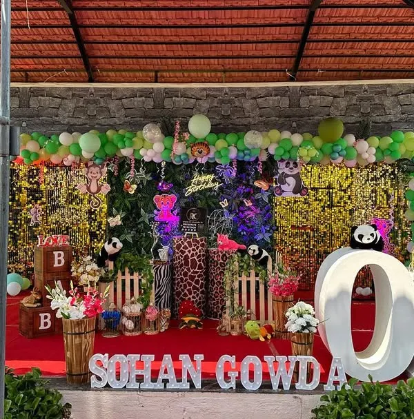 A grand outdoor jungle safari theme for a first birthday. This elaborate setup includes a gold shimmer wall, lush greenery, multiple animal cutouts, and giant 'ONE' marquee letters.