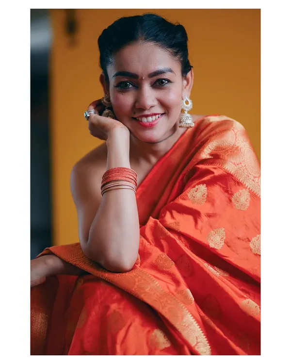 A warm and joyful portrait in a vibrant orange saree. The yellow background and the subject's bright smile create an image that is full of life and color, celebrating traditional Indian fashion.