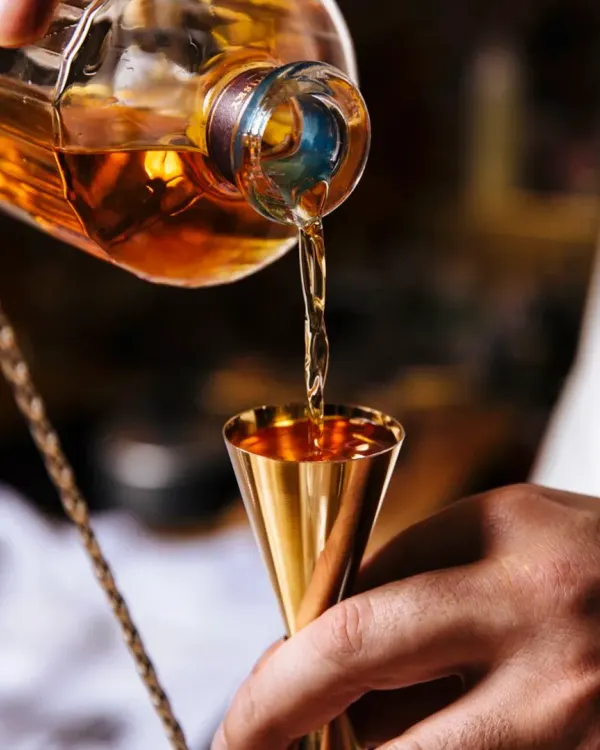 The perfect pour of whiskey into a golden jigger. This is where every great cocktail begins, with precision, quality ingredients, and a touch of craft.