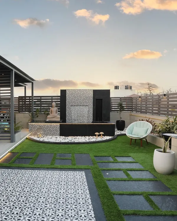 Peace and tranquility, right on your rooftop. This space features a modern water feature with a calming cascade, a serene Buddha statue, and a comfortable chair for quiet contemplation.