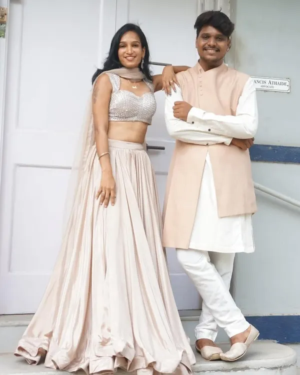 A classic his and her look. She’s in a flowing satin lehenga with a sequin blouse, and he’s in a complementary peach bandhgala jacket over a white kurta. Simple, elegant, and perfectly coordinated.