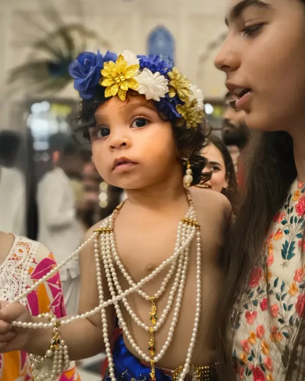 A close up portrait of a young child dressed as Lord Krishna for Janmashtami, looking directly into the camera with wide, innocent eyes.