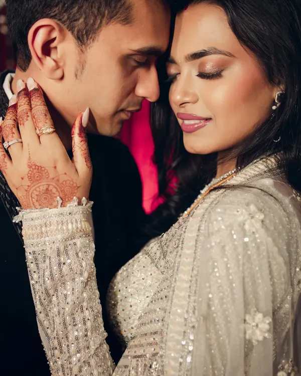An intimate close-up capturing the tender chemistry between the couple. The focus on the bride's henna-adorned hand gently touching his neck adds a layer of traditional romance to this modern, glamorous shot.