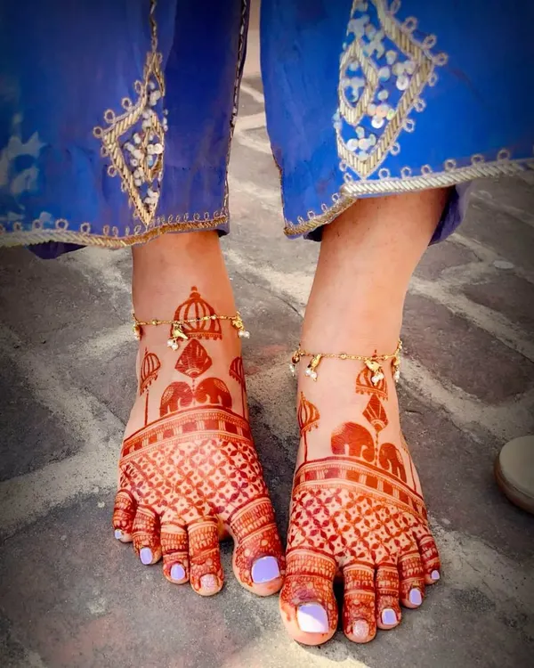 The beautiful dark stain of a bridal foot mehndi design. This pattern features traditional elephant and dome motifs with a delicate checkered pattern on the toes.