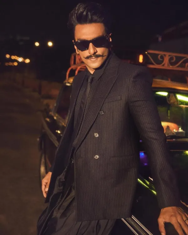 Ranveer Singh embodying the 'Desi Kalakar' vibe for the Jio World Plaza opening. This look features a sharp pinstripe YSL blazer paired with draped Manish Malhotra pants and boots, creating a fusion of global and Indian aesthetics.