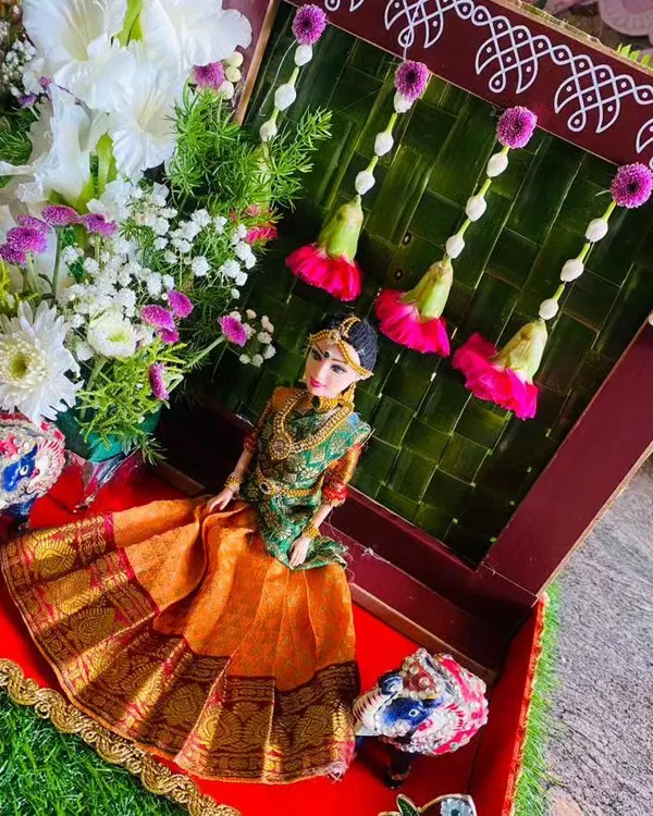 A beautiful gift platter we designed for a half saree ceremony. It features a doll dressed in a traditional orange and green saree, set against a backdrop of woven palm leaves and fresh flowers.