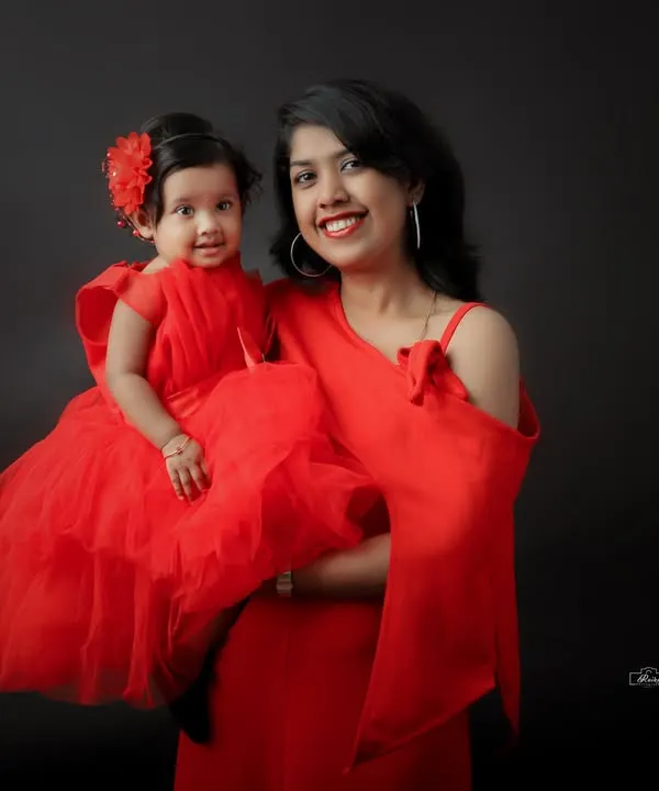 A striking mother and daughter portrait with matching red dresses against a classic dark backdrop. This studio shot emphasizes connection and style, creating a bold and beautiful memory.