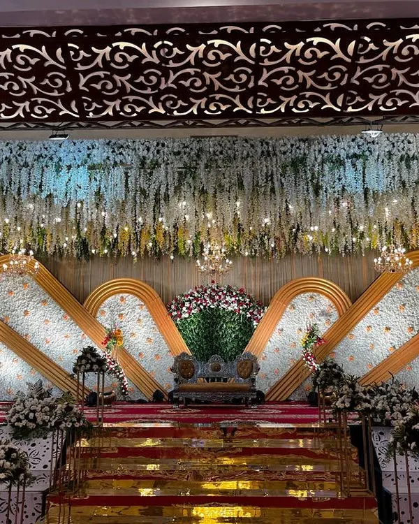 This grand reception stage in Hassan features a stunning backdrop made of thousands of white flowers. The design uses layered panels and a ceiling of hanging florals, all illuminated to create a truly luxurious and photogenic setting.