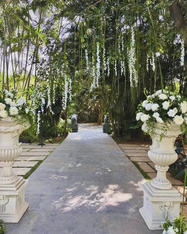 A breathtaking wedding aisle lined with white floral urns and a canopy of hanging white wisteria, creating a path straight out of a fairytale.