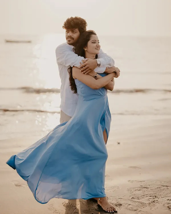 A beautiful golden-hour portrait on the beach, with the wind catching the bride's dress as the couple embraces by the sea.