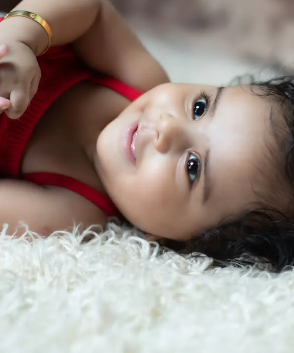 A beautiful close-up of a happy baby girl with sparkling eyes and curly hair, lying on a soft white rug.