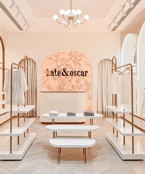 For the Kate & Oscar kids' boutique, we designed a serene and whimsical retail experience. This wide view captures the harmony of custom rose gold arches, clean white shelving, and a soft, inviting color palette, all working together to create a calm journey for shoppers.