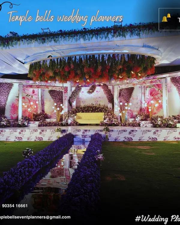 A grand reception stage we designed, featuring a dramatic overhead floral chandelier, a mirrored aisle, and lush purple flower arrangements for a truly royal feel. This setup showcases our expertise in large scale event production and floral design.
