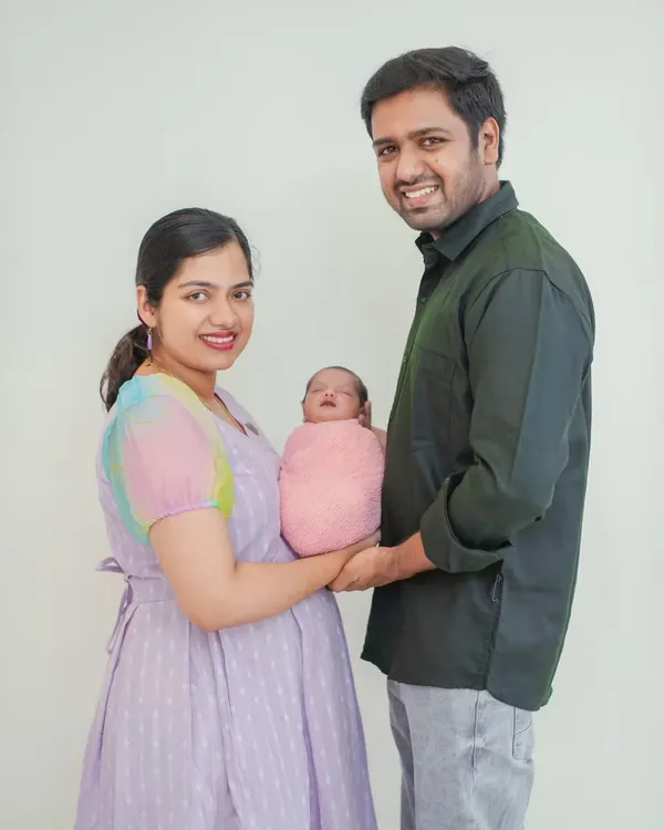 A classic family portrait with both parents holding their newborn. The clean white background keeps the focus entirely on the family's happy moment together.