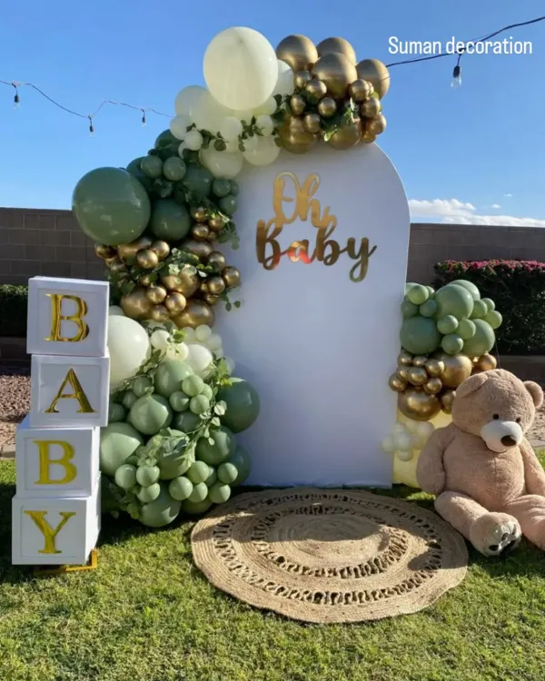 A beautiful outdoor baby shower setup with a modern, rustic feel. I used a balloon arch in sage green, white, and gold, along with "BABY" blocks and a large teddy bear.