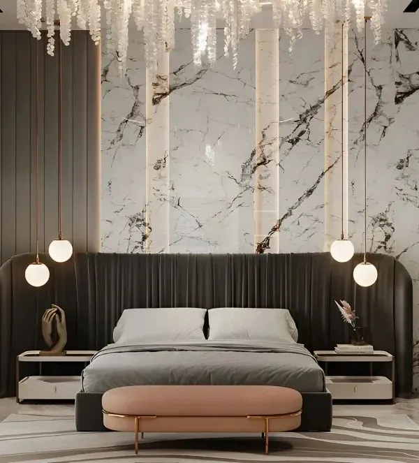 A luxurious master bedroom featuring a floor-to-ceiling upholstered headboard against a stunning marble accent wall. The design is completed with cascading pendant lights and a chic pink bench.